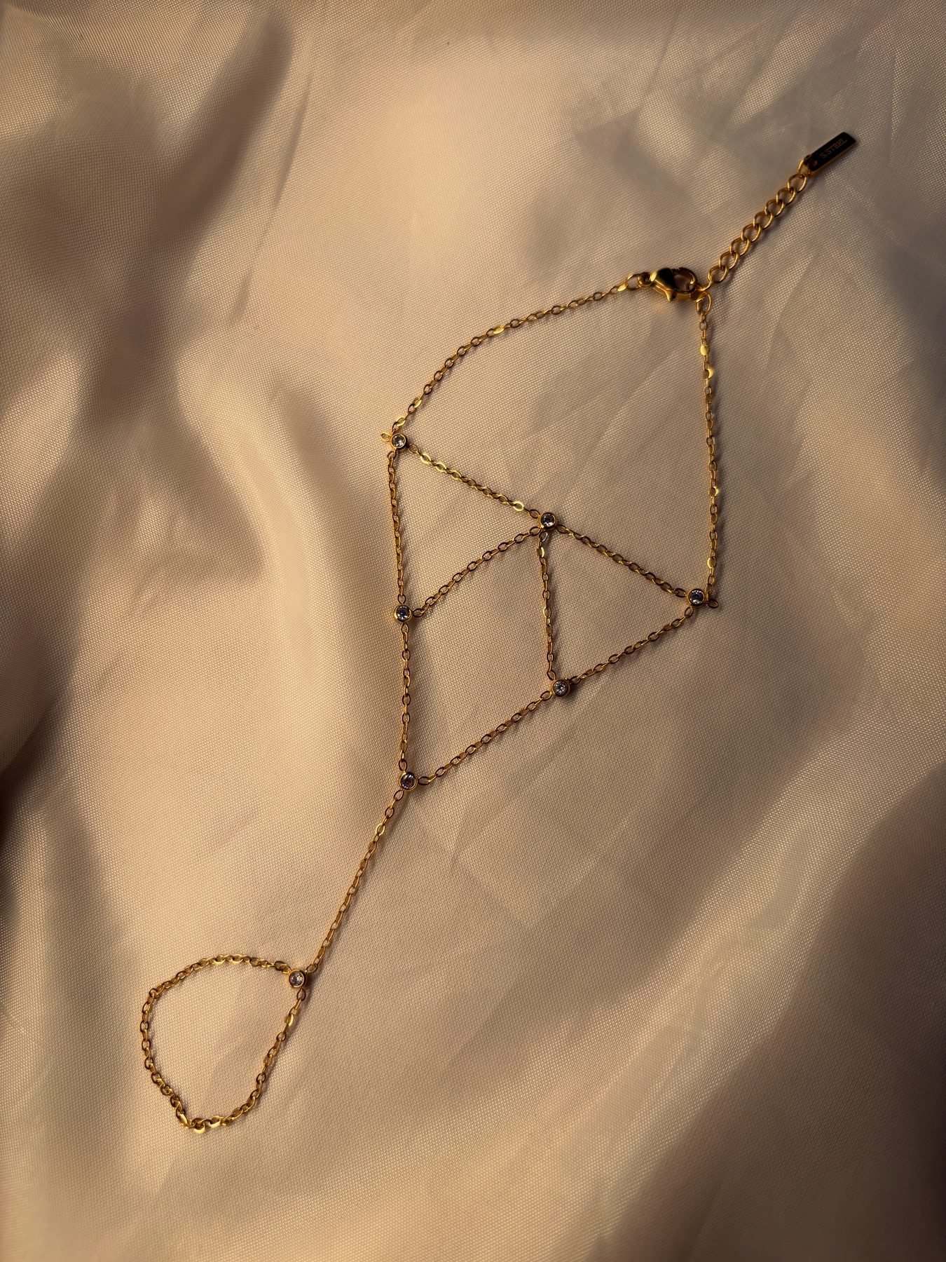 The Glossy Hand Chain on cream silk showing its lattice of fine gold chain